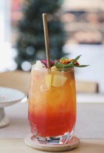 Colorful fruit cocktail garnished with mint and flowers, set on a table indoors.