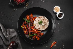 A tantalizing Asian stir-fry with chicken and vegetables beside seasoned rice on a black plate.
