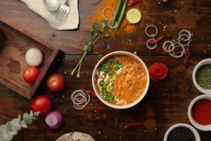 A vibrant top-down view of a flavorful Indian curry surrounded by fresh vegetables and spices.