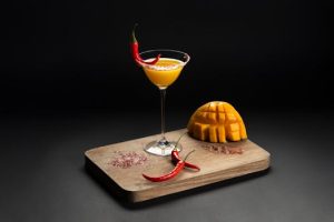 Refreshing mango cocktail garnished with red chili peppers on a wooden board, a unique blend of flavors.