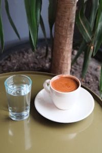 A cozy setup with a cup of espresso and water on a table by a plant indoors.