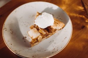 A delicious slice of apple pie topped with whipped cream on a rustic ceramic plate.
