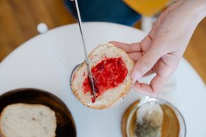 Hand spreading raspberry jam on fresh bread beside a cup of tea. Perfect for breakfast scenes.