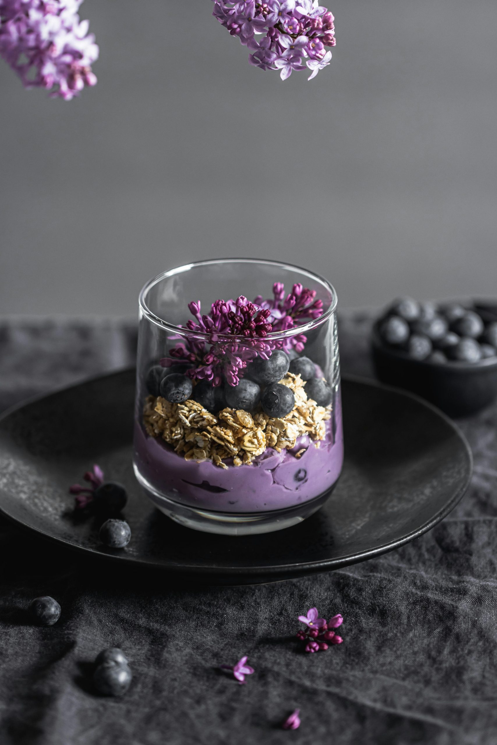 A stylish vertical shot of a blueberry granola parfait with lilac flowers.
